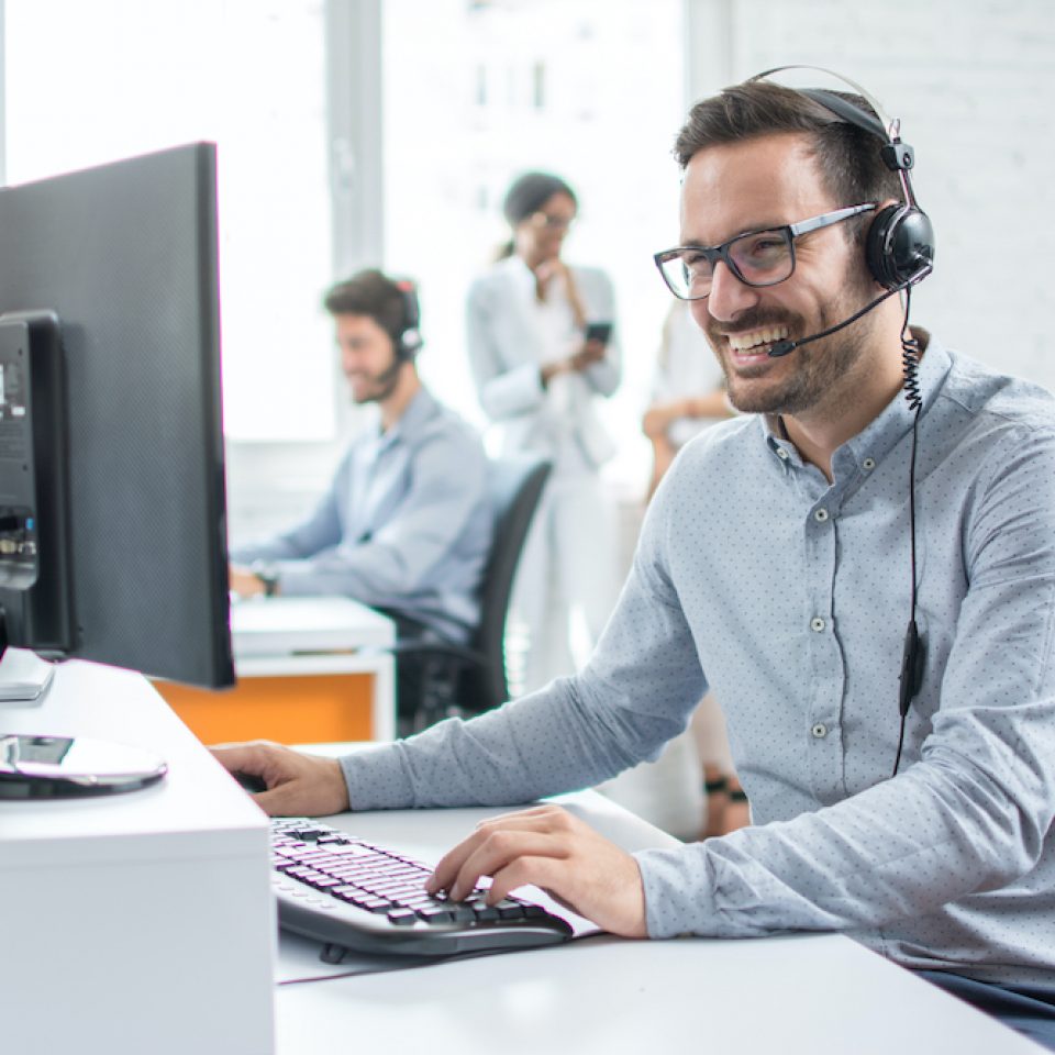 Smiling customer support operator with hands-free headset working in the office.