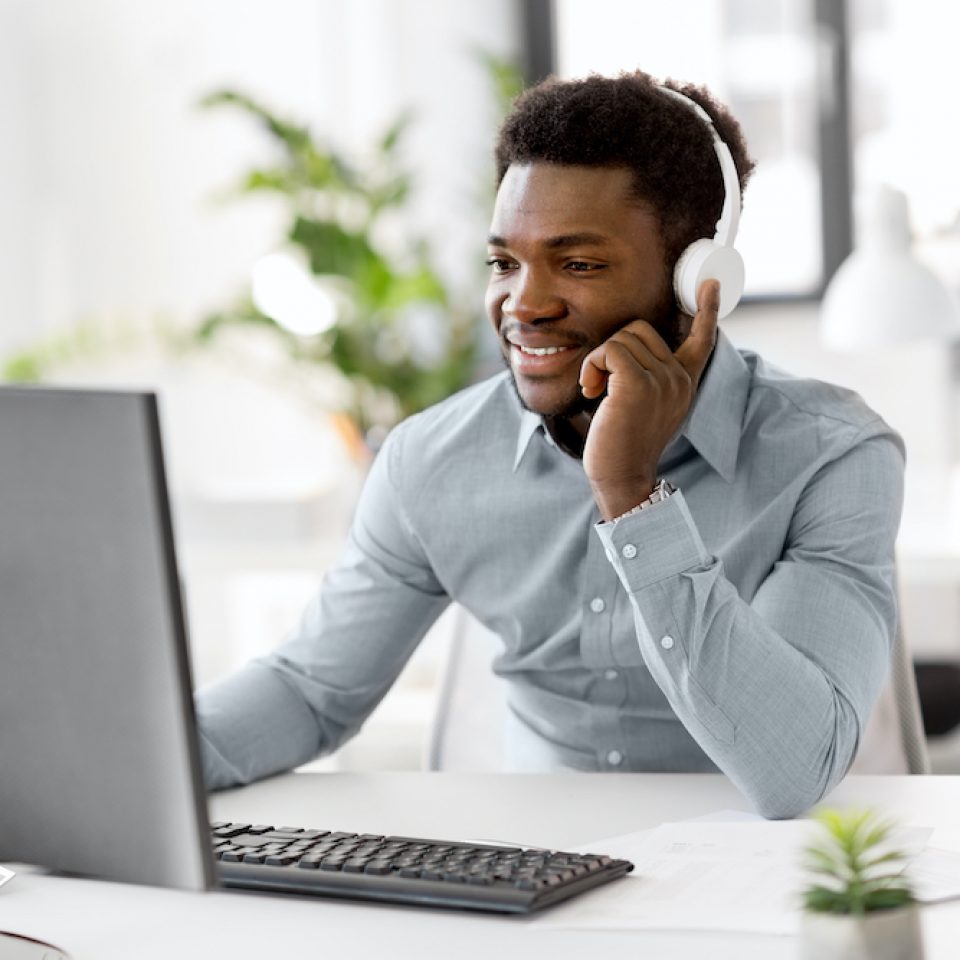 business, technology and people concept - happy african american businessman with headphones and computer computer listening to music at office